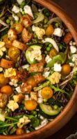 A salad with vegetables, cheese, croutons and flowers in a wooden bowl.