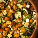 A salad with vegetables, cheese, croutons and flowers in a wooden bowl.