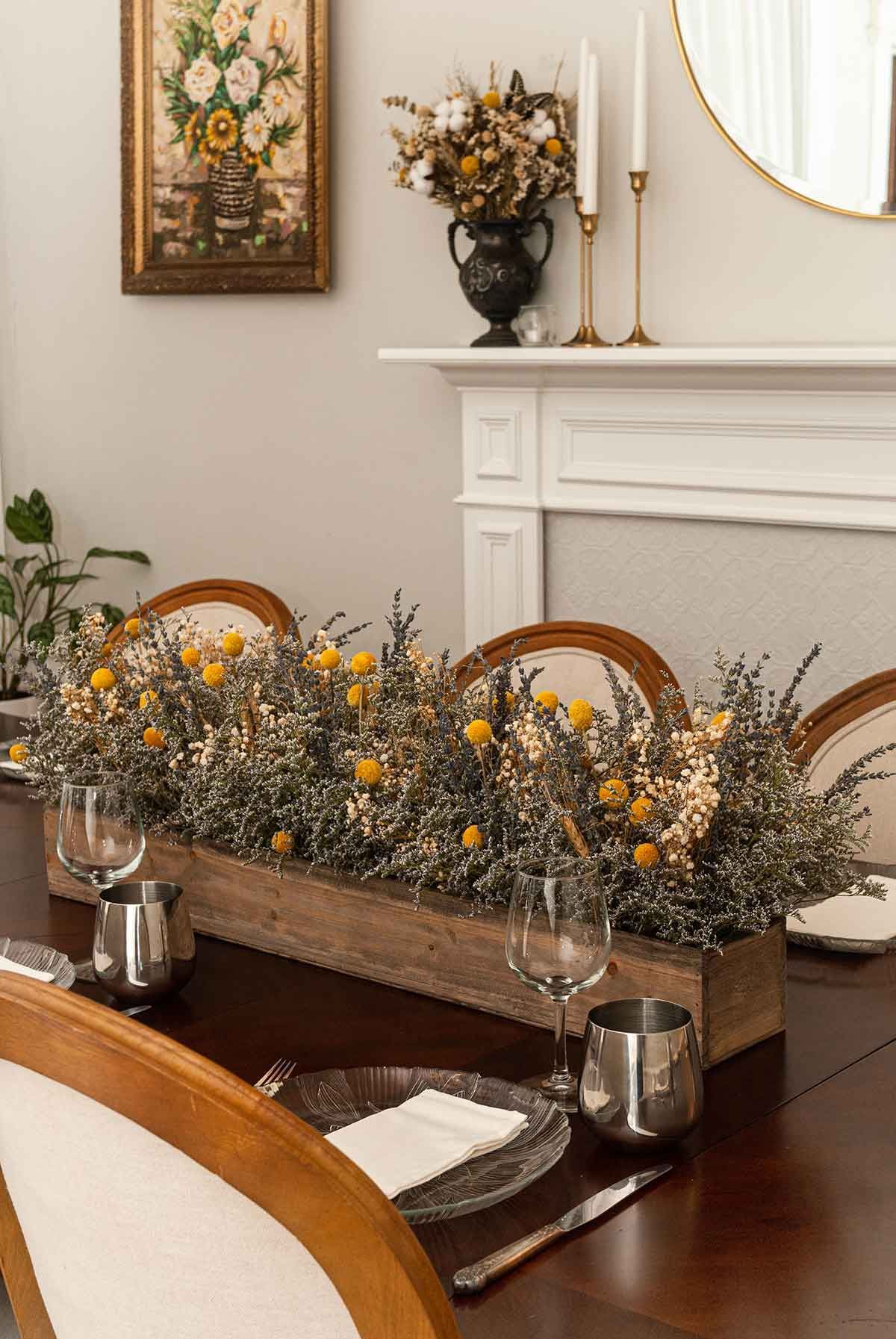 A dry flower box centerpiece on a table set with plates, glasses and cutlery.