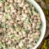 Chickpea salad with dill on a lace tablecloth surrounded by flowers.