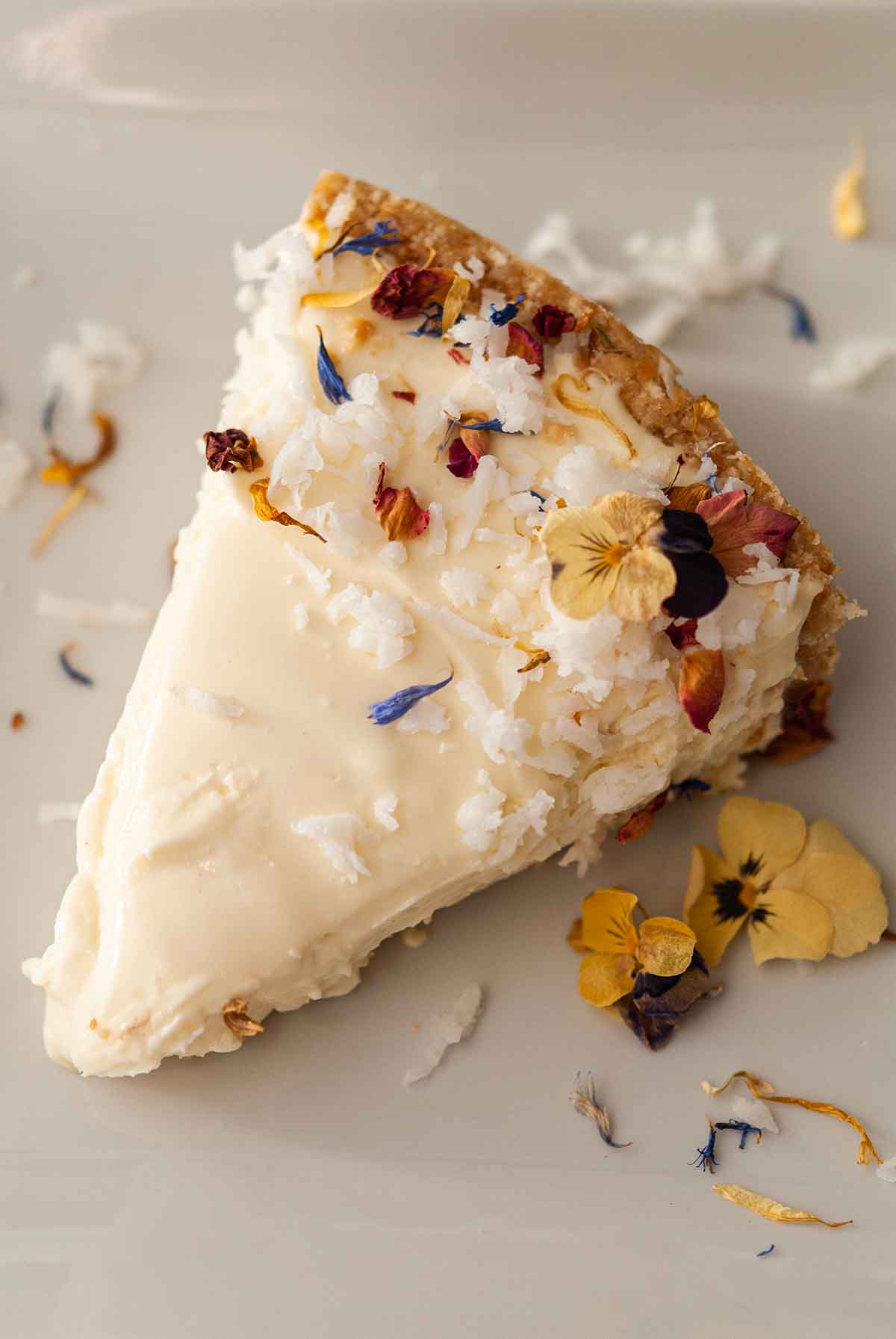 A coconut cheesecake slice garnished with coconut and flowers on a plate.