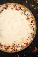 A coconut cheesecake garnished with flowers and coconut on a table sprinkled with flowers.