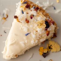 A coconut cheesecake slice garnished with coconut and flowers on a plate.