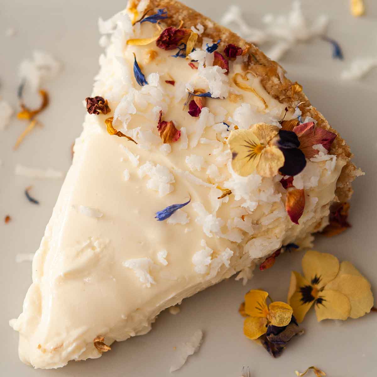 A coconut cheesecake slice garnished with coconut and flowers on a plate.