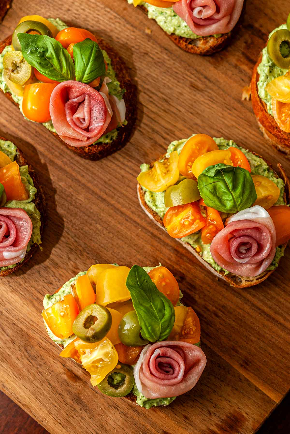 6 pesto crostini with a prosciutto rose on a wooden board.