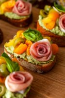 4 pesto crostini with prosciutto roses on a wooden board.