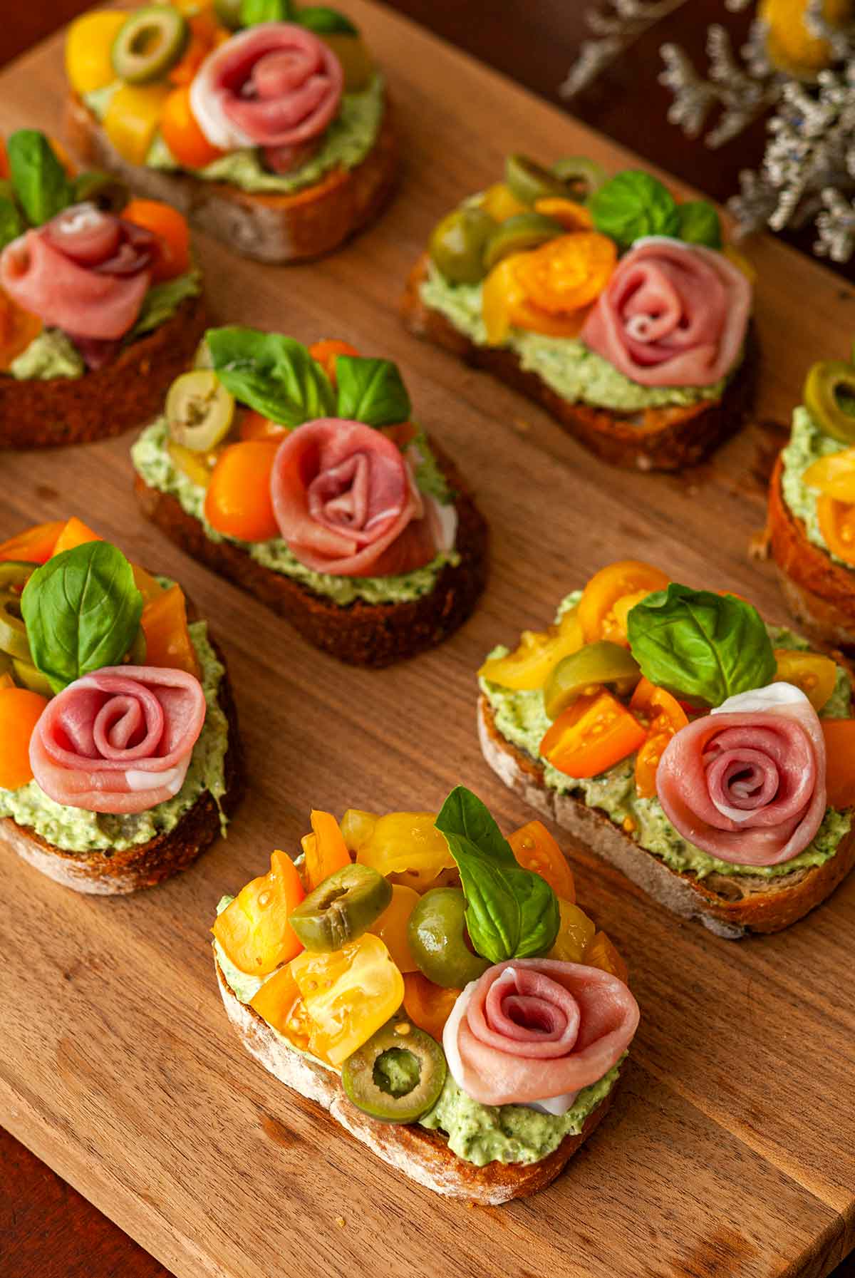 8 pesto crostini with prosciutto roses on a wooden board.