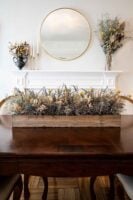 A dry flower box centerpiece on a table in front of a decorative fireplace and flowers.