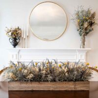 A dry flower box centerpiece on a table in front of a decorative fireplace and flowers.