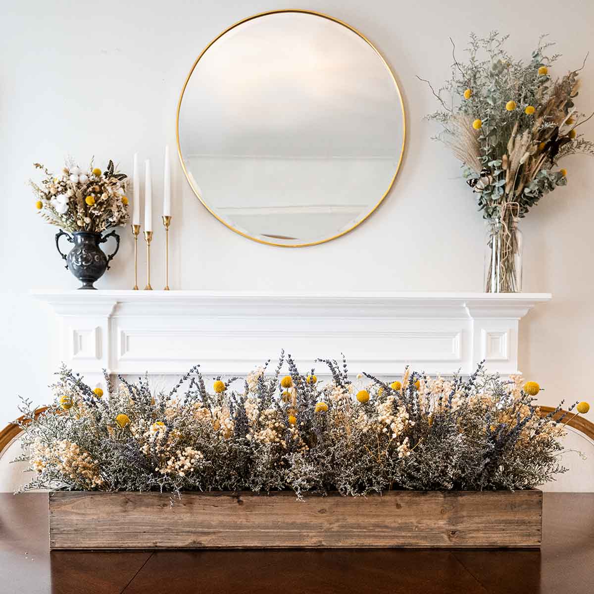 A dry flower box centerpiece on a table in front of a decorative fireplace and flowers.