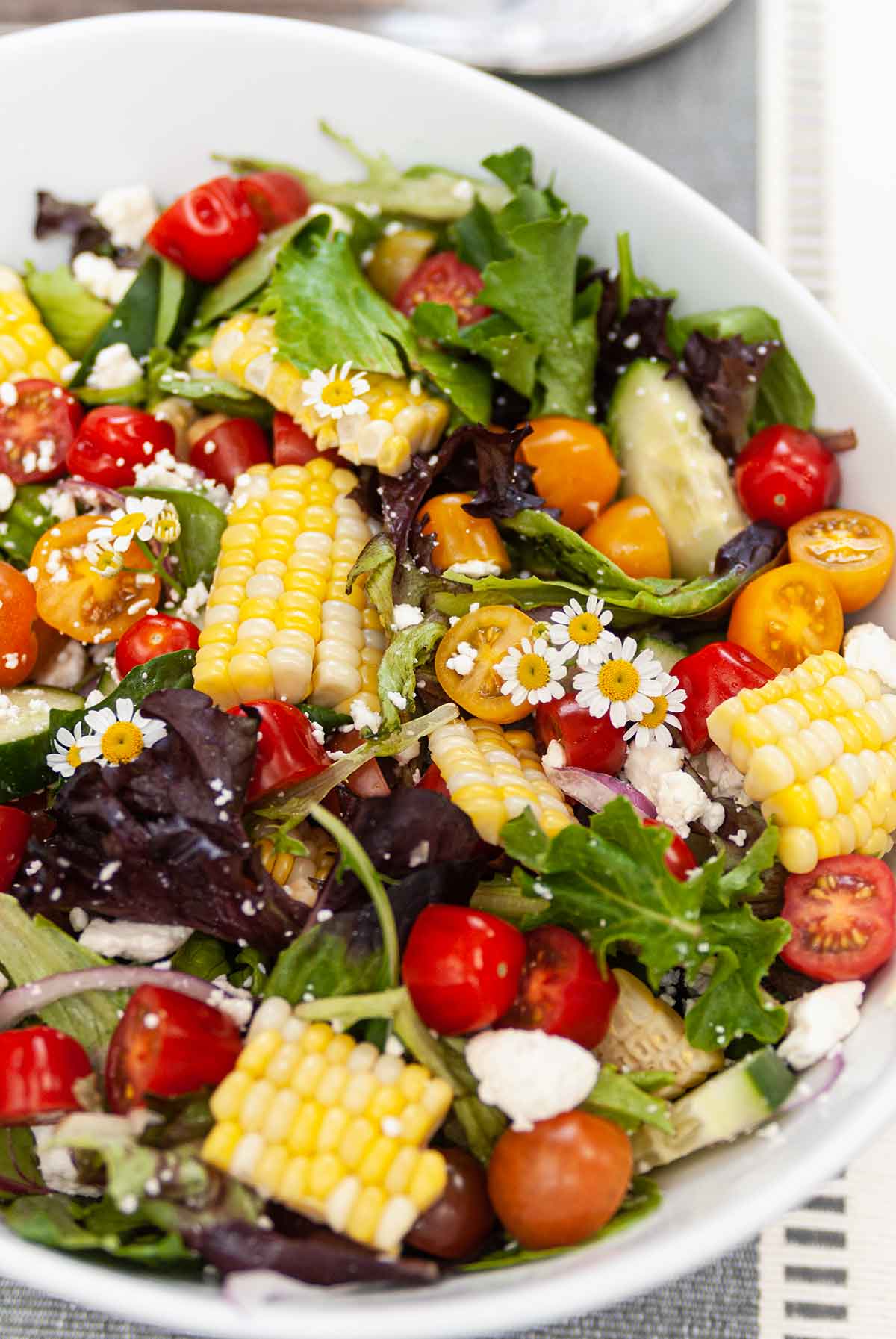 A bowl of summer corn salad with slices of corn and small flowers on a table.