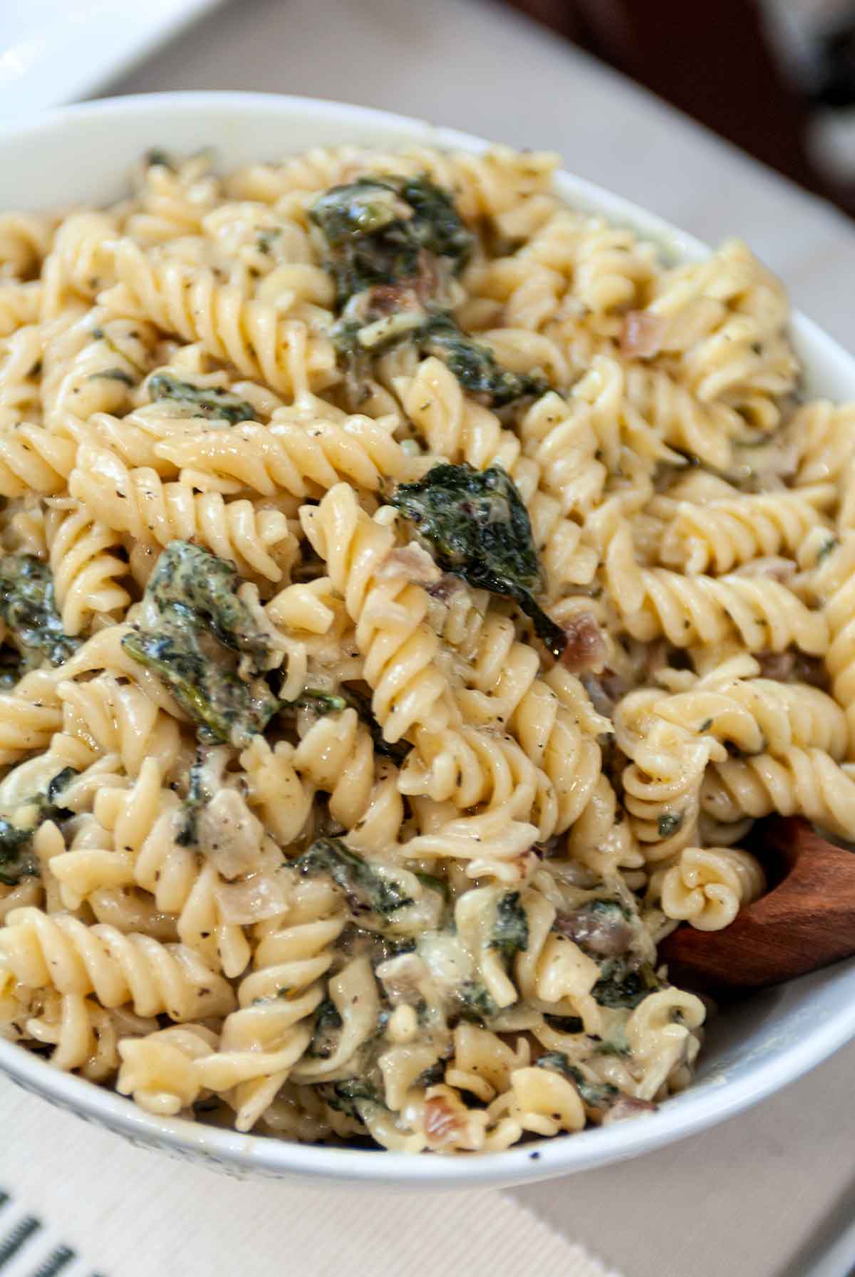 A bowl full of pasta with spinach with a wooden spoon.