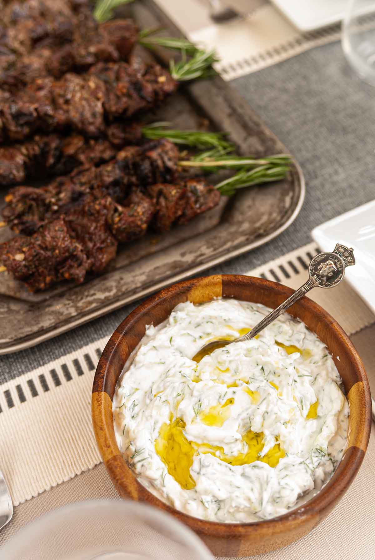 A bowl of tzatziki beside lamb skewers on a rustic platter.