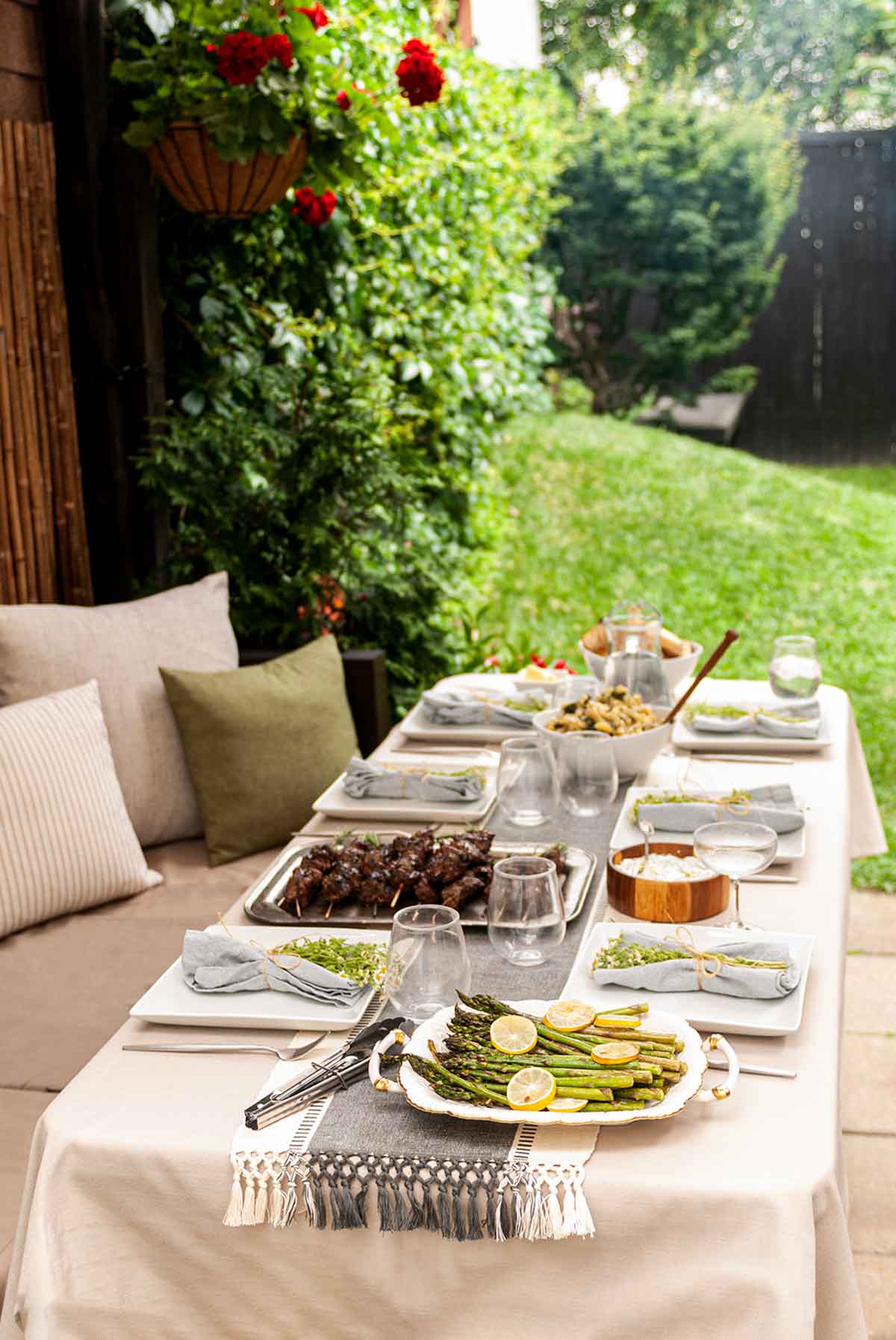 A table in a back yard garden with seasonal food on the table cloth of a table.