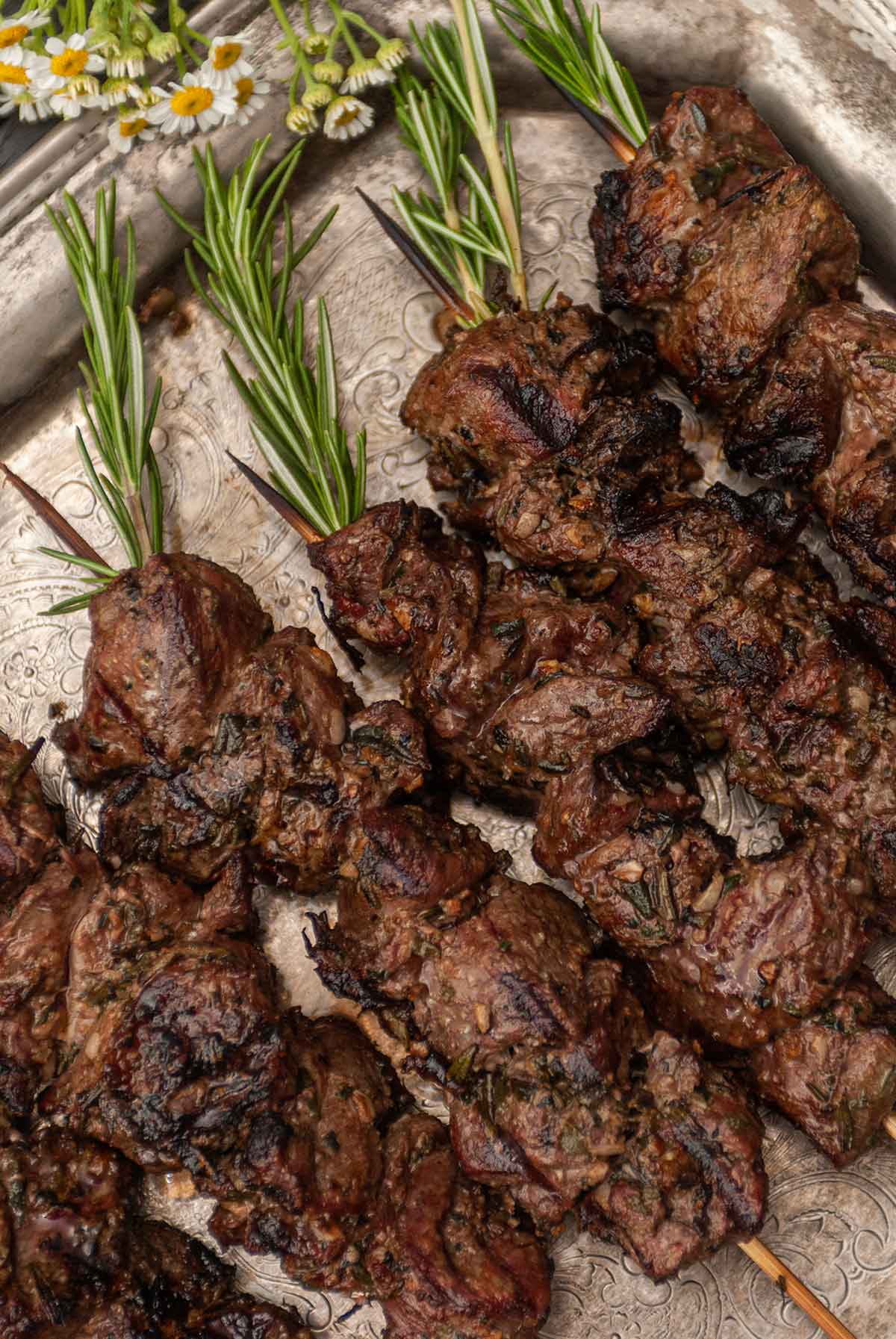 Lamb skewers with rosemary tops on a rustic platter.