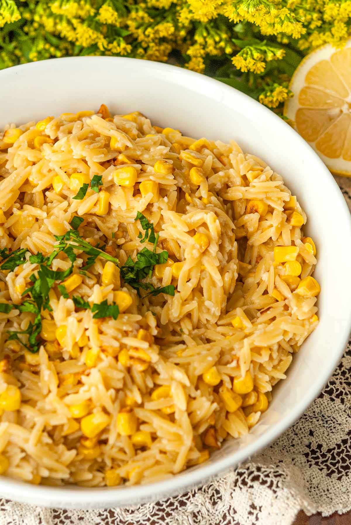 A bowl of lemon orzo on a lace table cloth with flowers in the background.