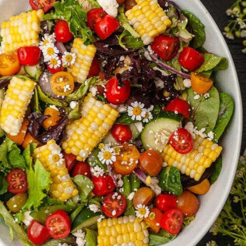 A bowl of brightly colored corn salad with little flowers.