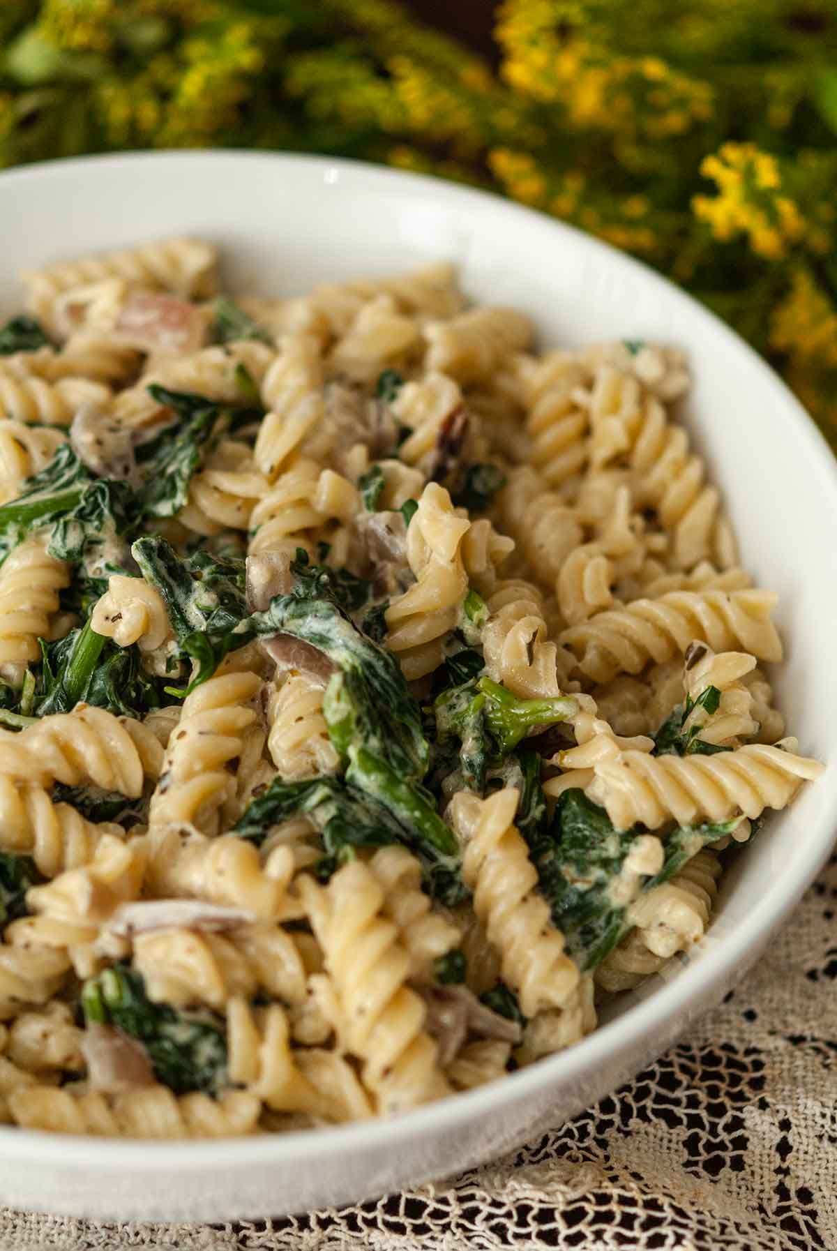 A bowl of pasta with spinach on a table with flowers.