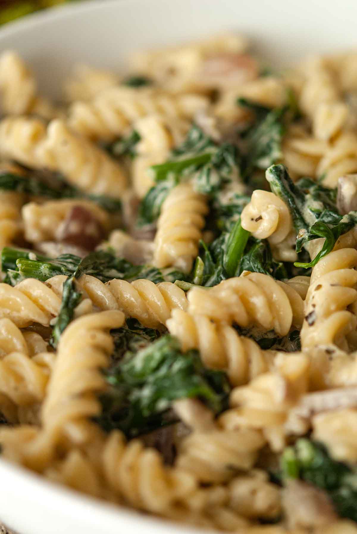 Cheesy pasta with spinach and red onion in a bowl.