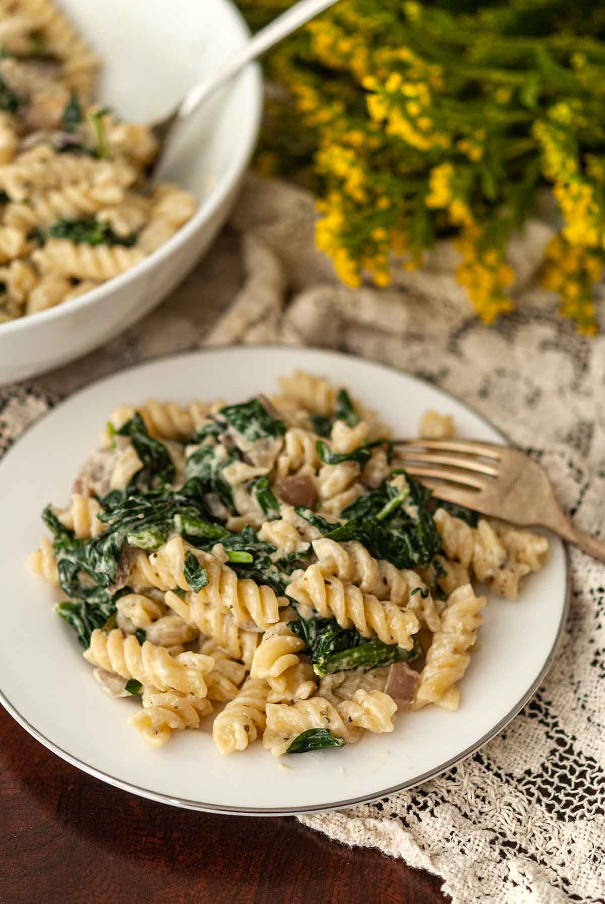 A plate of tuscan pasta beside a bowl on lace beside flowers.