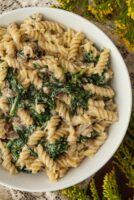 A bowl of pasta with spinach on a lace table cloth beside flowers