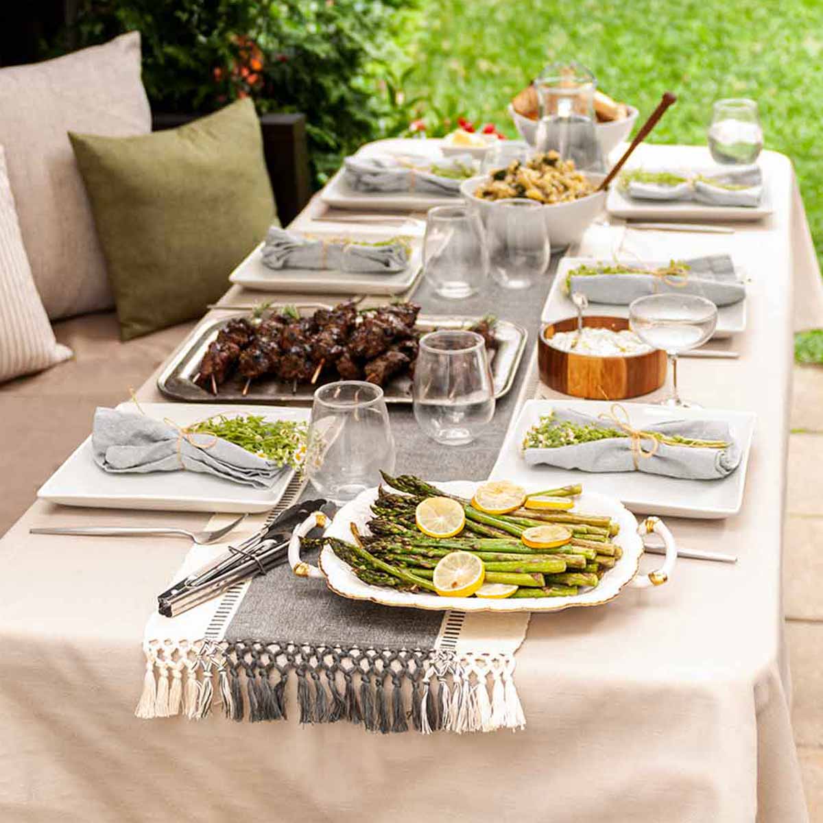 A table in a back yard garden with seasonal food on the table cloth of a table.