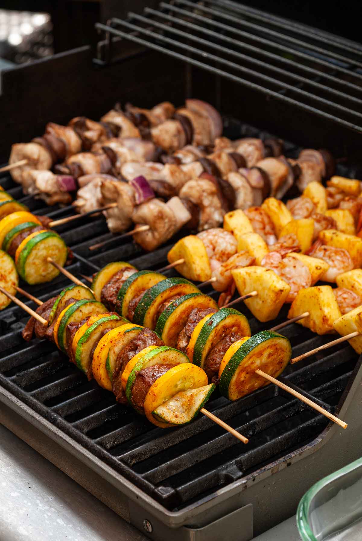 12 meat and vegetable skewers on a grill.