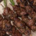 Lamb skewers with rosemary tops on a rustic platter.