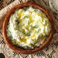 A bowl of tzatziki, drizzled with olive oil, on a lace tablecloth.