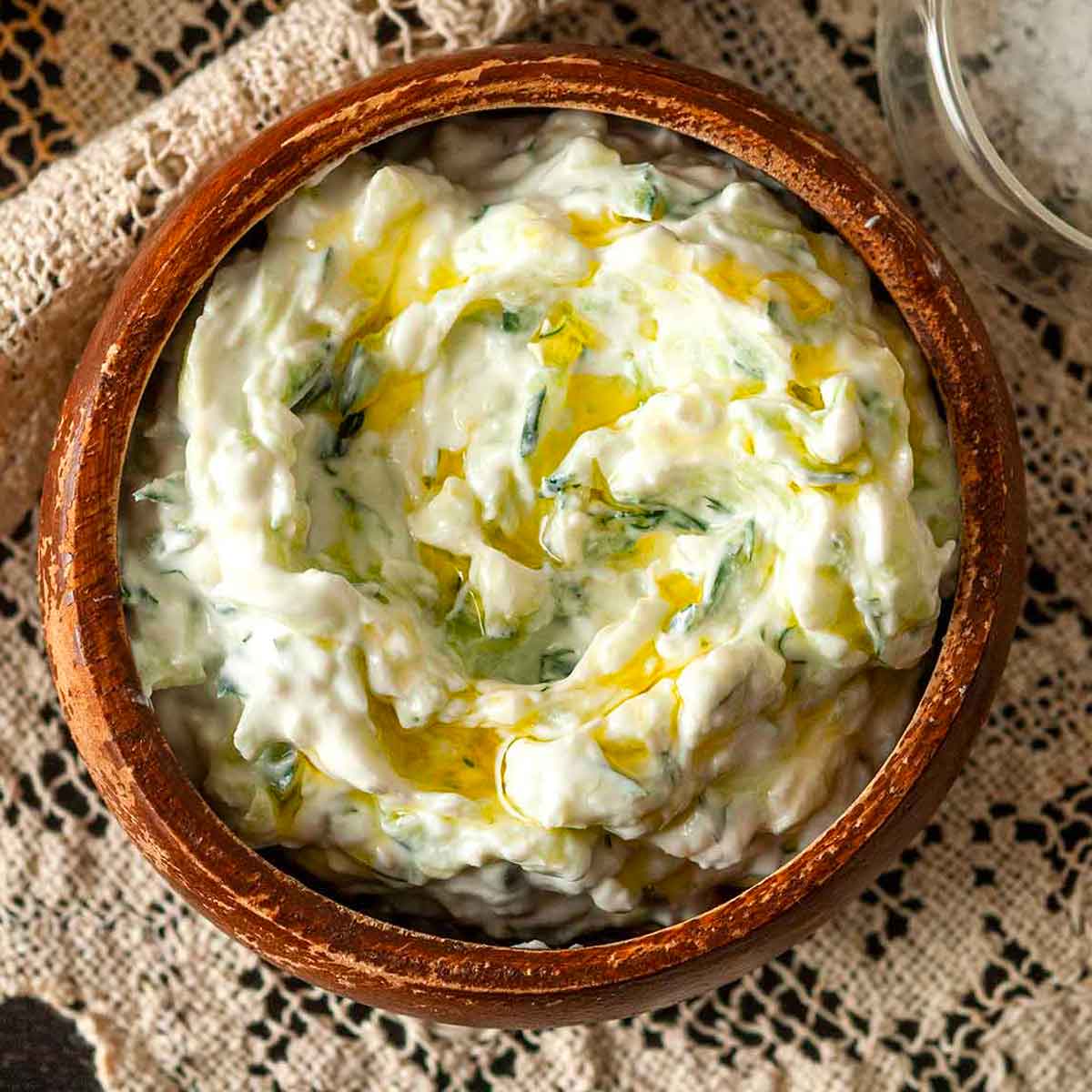 A bowl of tzatziki, drizzled with olive oil, on a lace tablecloth.