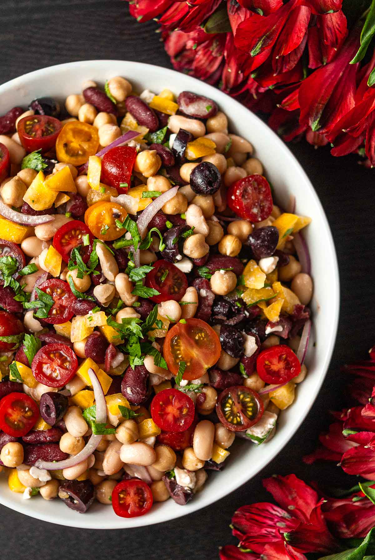 A bowl of Italian 3 bean salad in a bowl beside flowers.
