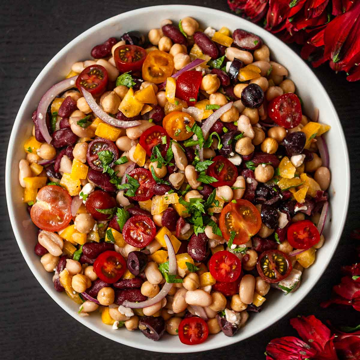 A bowl of Italian 3 bean salad in a bowl centered, beside flowers.