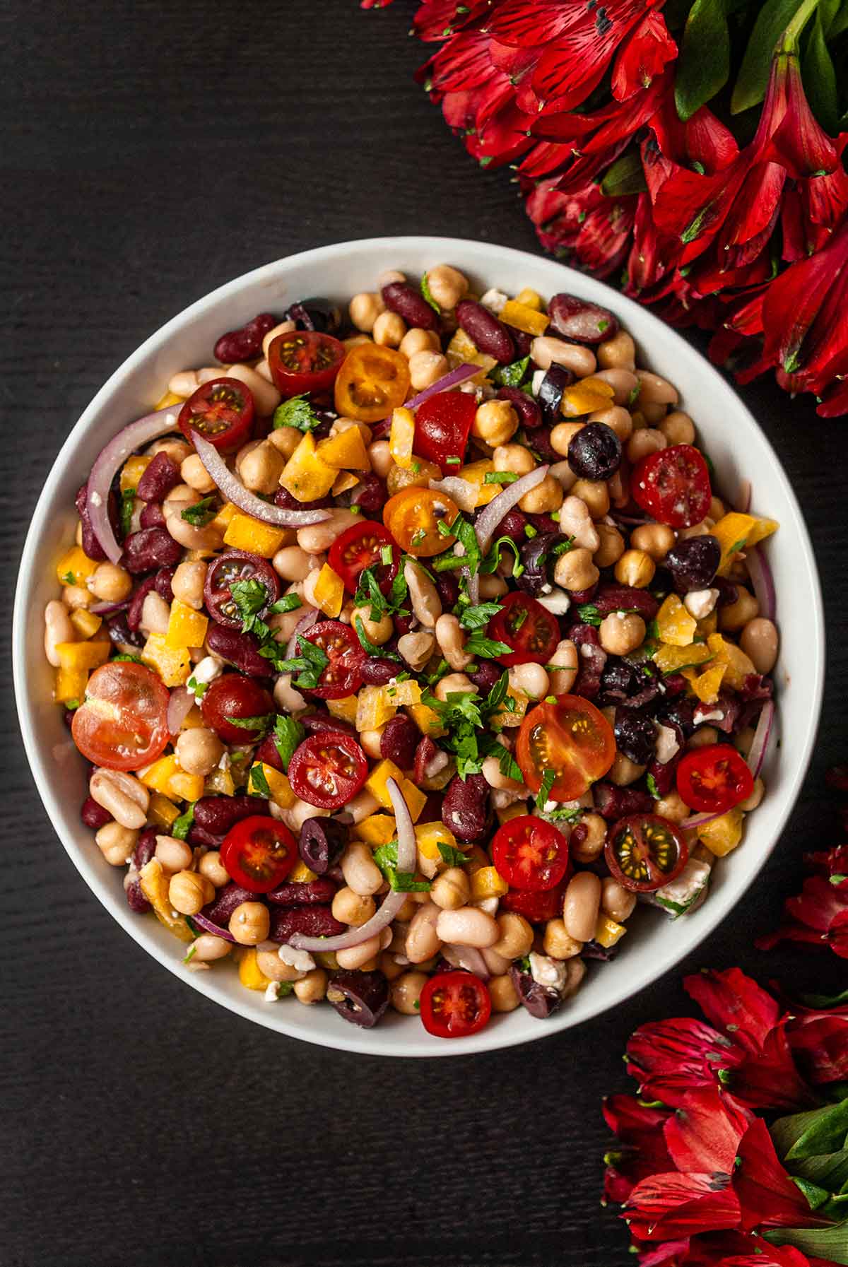 A bowl of Italian 3 bean salad in a bowl centered, beside flowers.