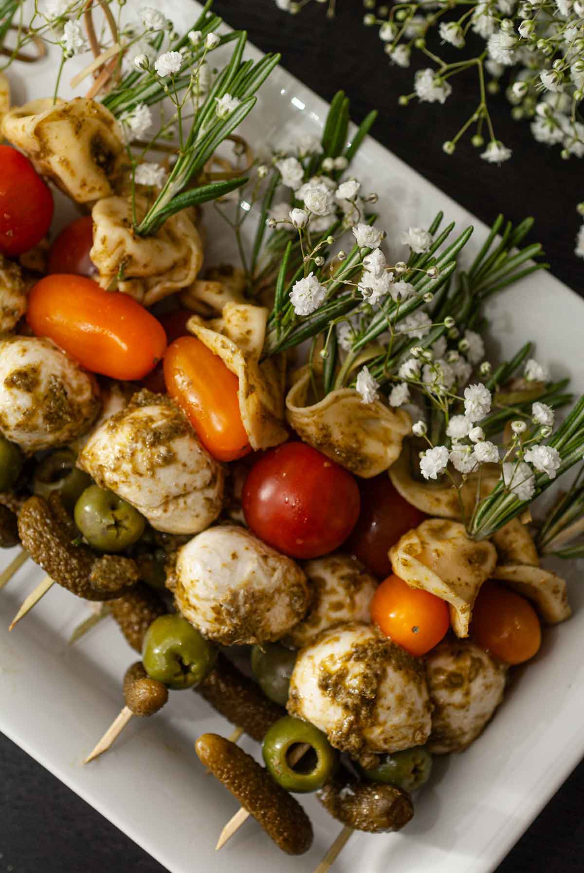 Antipasto skewers garnished with flowers and rosemary stacked on a plate.