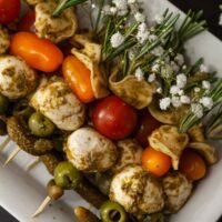 Antipasti skewers garnished with flowers and rosemary stacked on a plate.