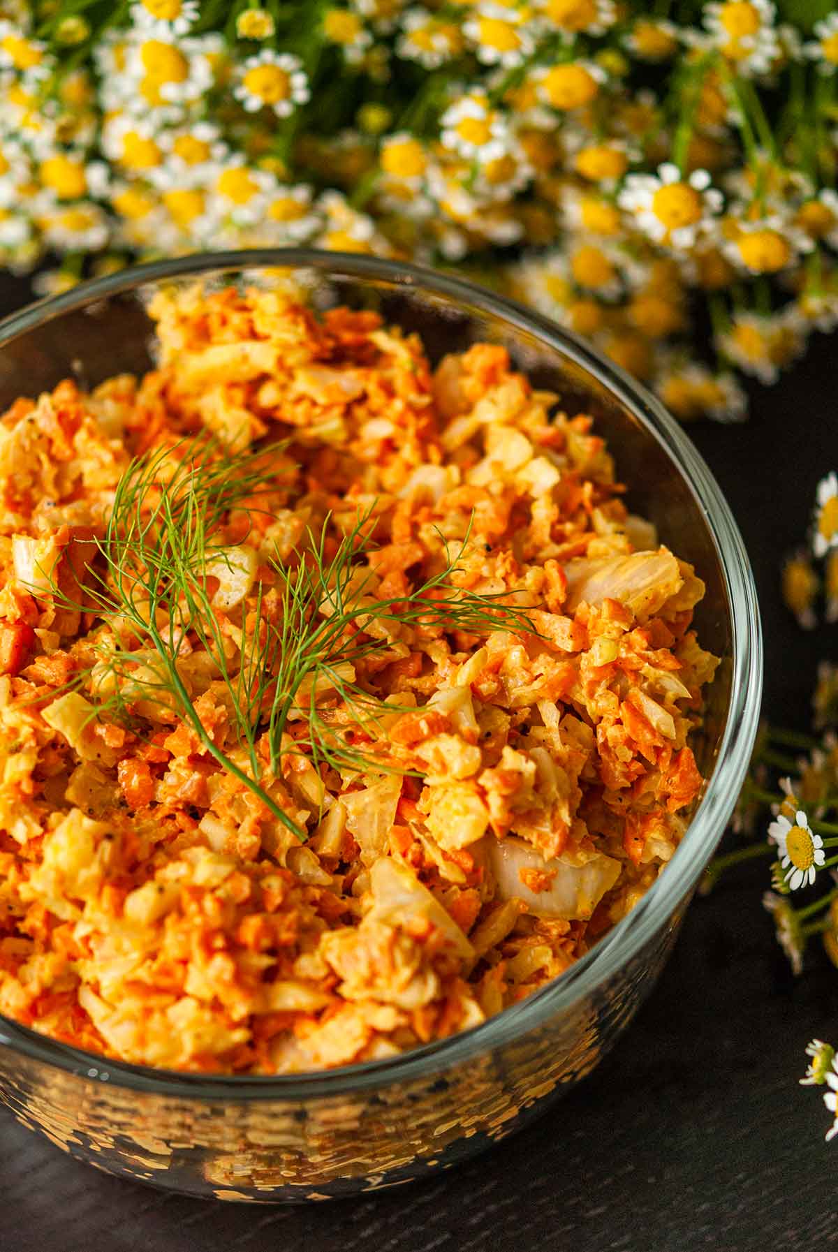 Curried coleslaw in a bowl beside flowers topped with fresh dill.