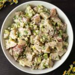 A bowl of dill potato salad centered on a table beside flowers.