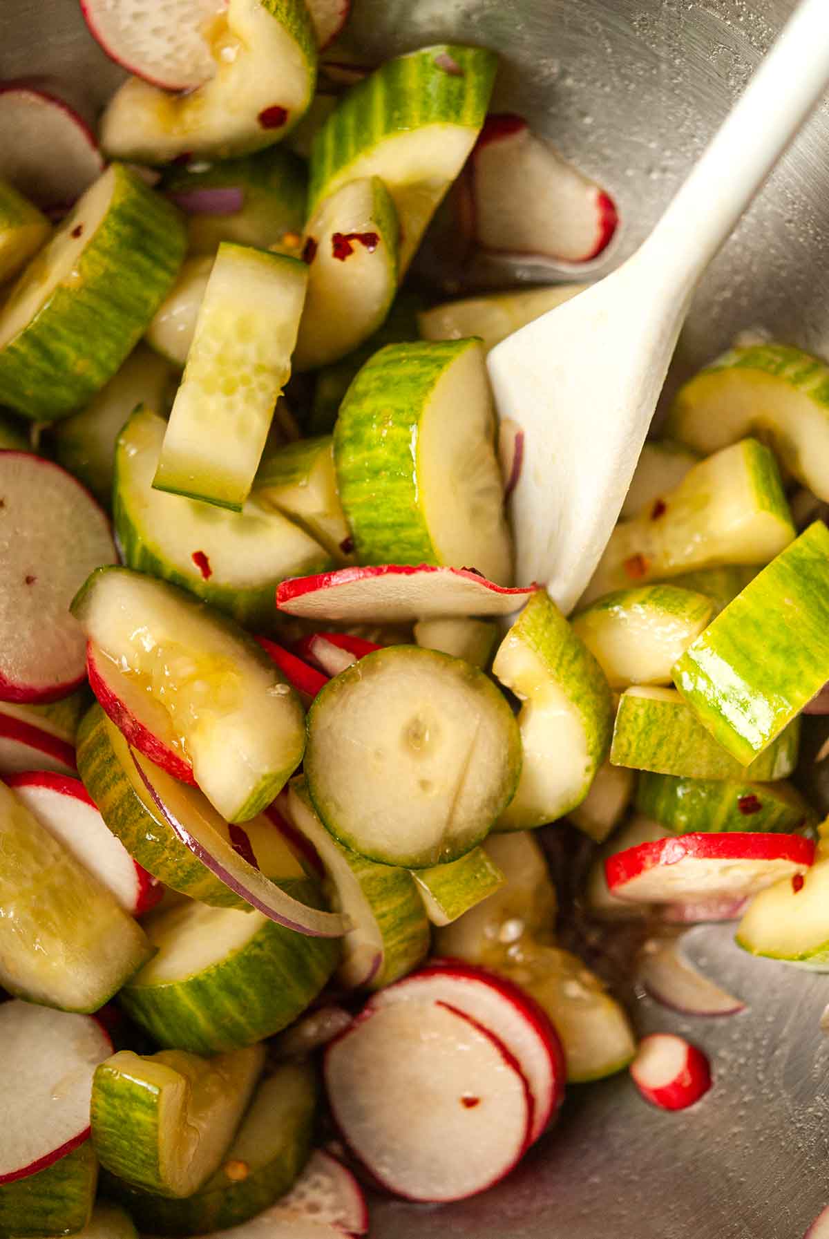 Cucumbers, radishes and onion with ponzu sauce in a mixing bowl.