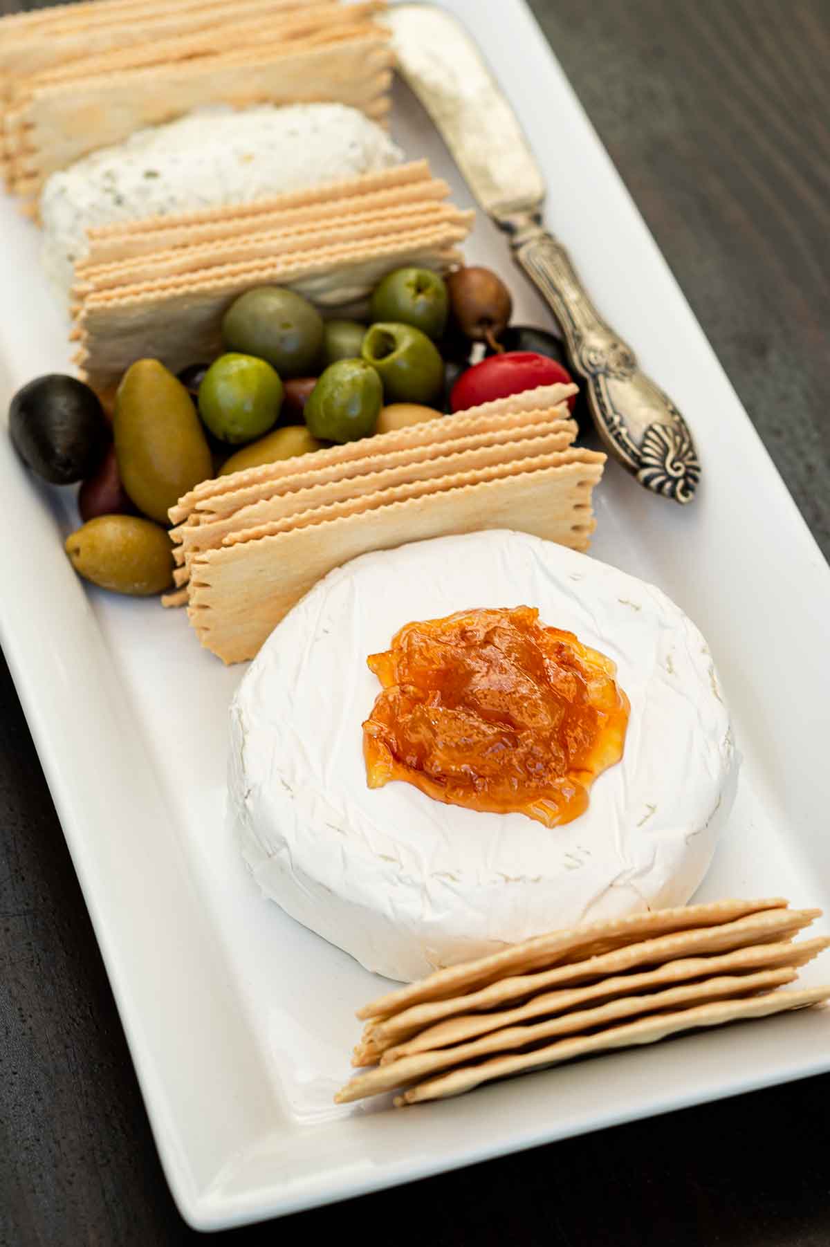 A cheese plate with crackers, olives and cheese topped with marmalade.