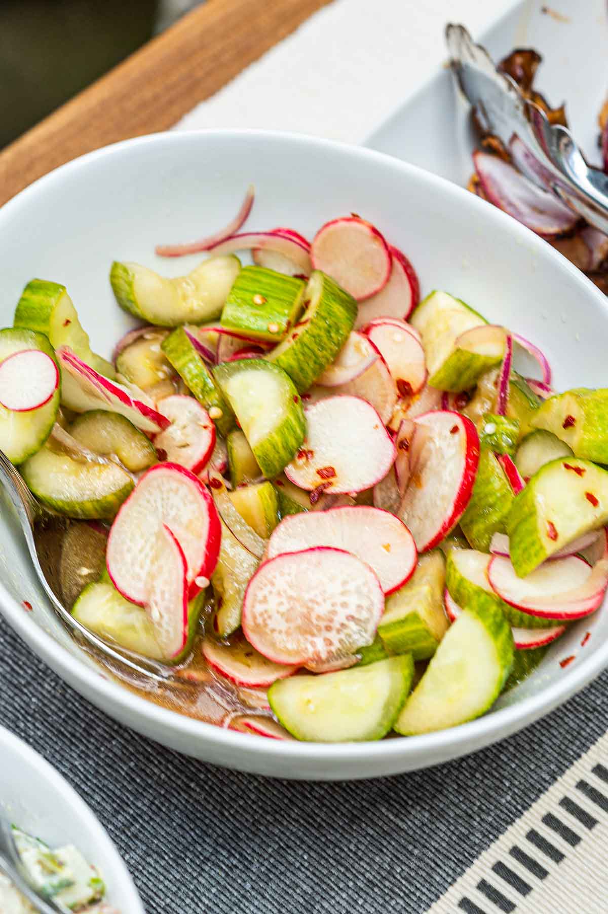 A bowl of ponzu cucumbers and radishes on a table.