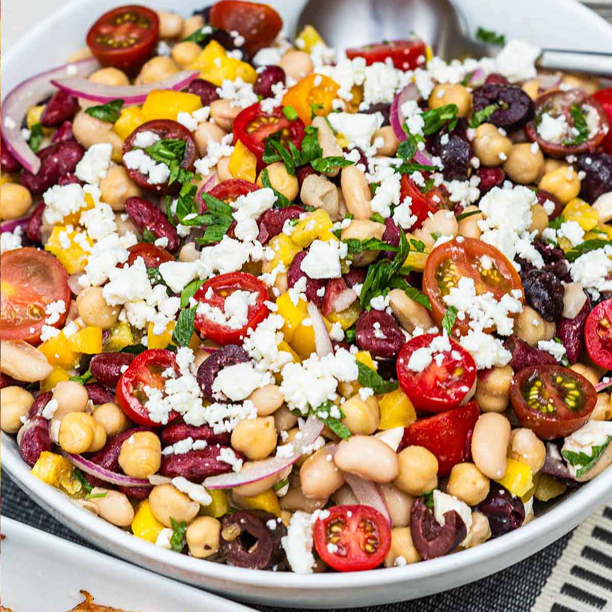 A bowl of 3 bean salad on a table, sprinkled with feta.