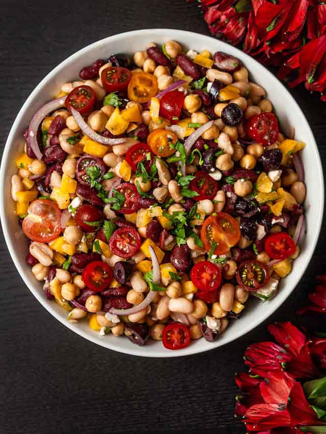 A bowl of Italian 3 bean salad in a bowl centered, beside flowers.