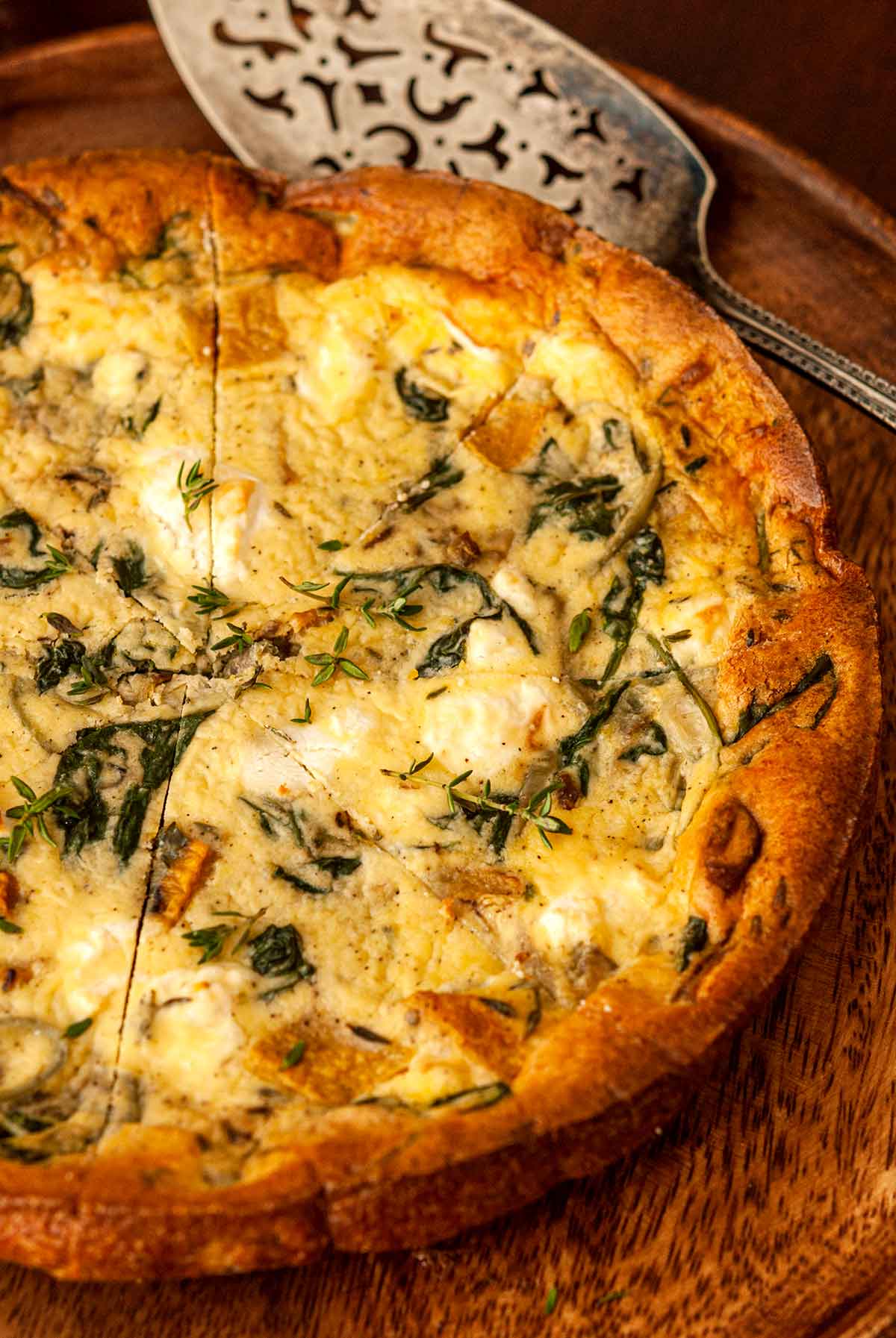 A quiche on a wooden plate with an antique pie server.