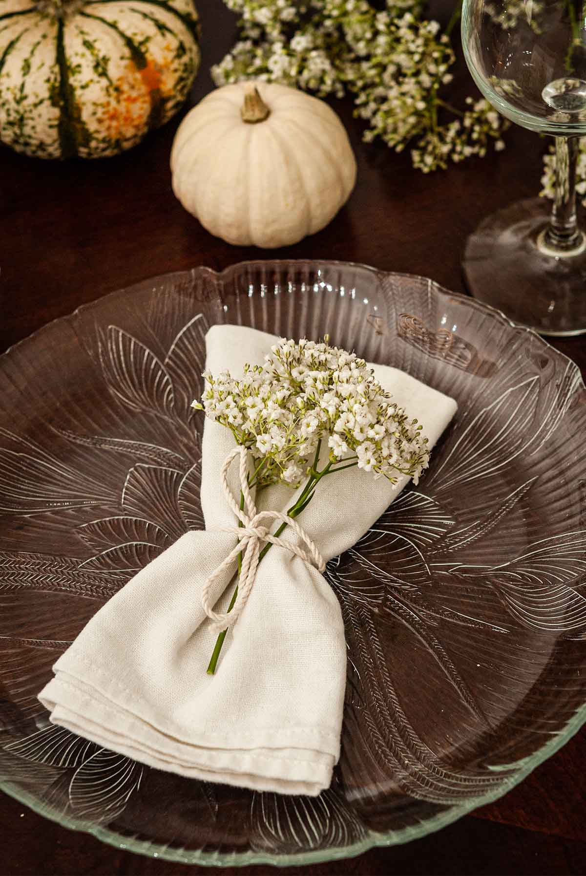 A plate with a napkin with flowers tied with string in front of small pumpkins and flowers on a table.
