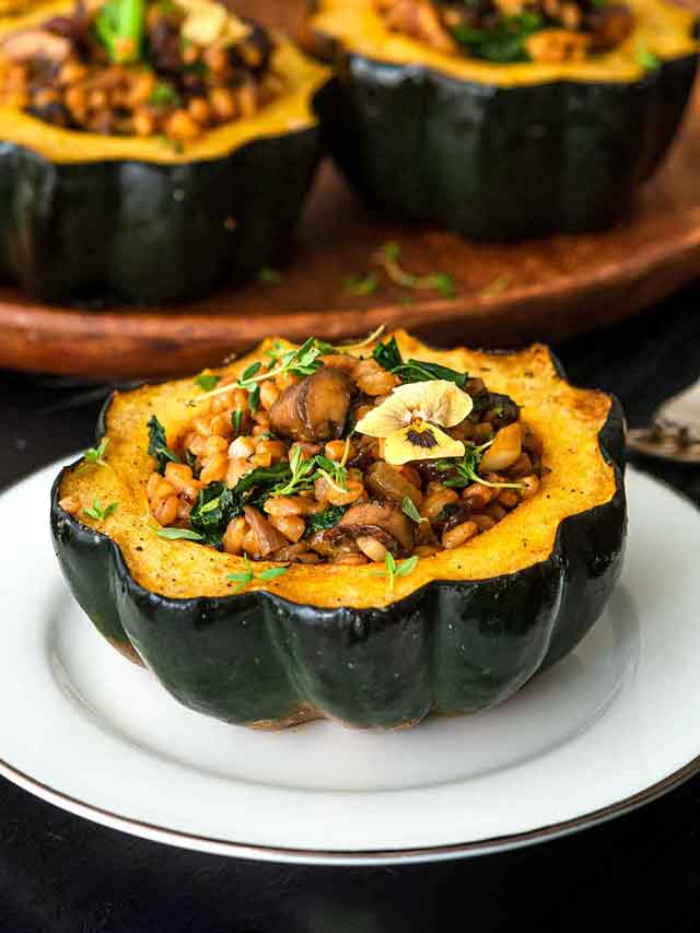 1 acorn squash on a plate in front of 2 others on a table.