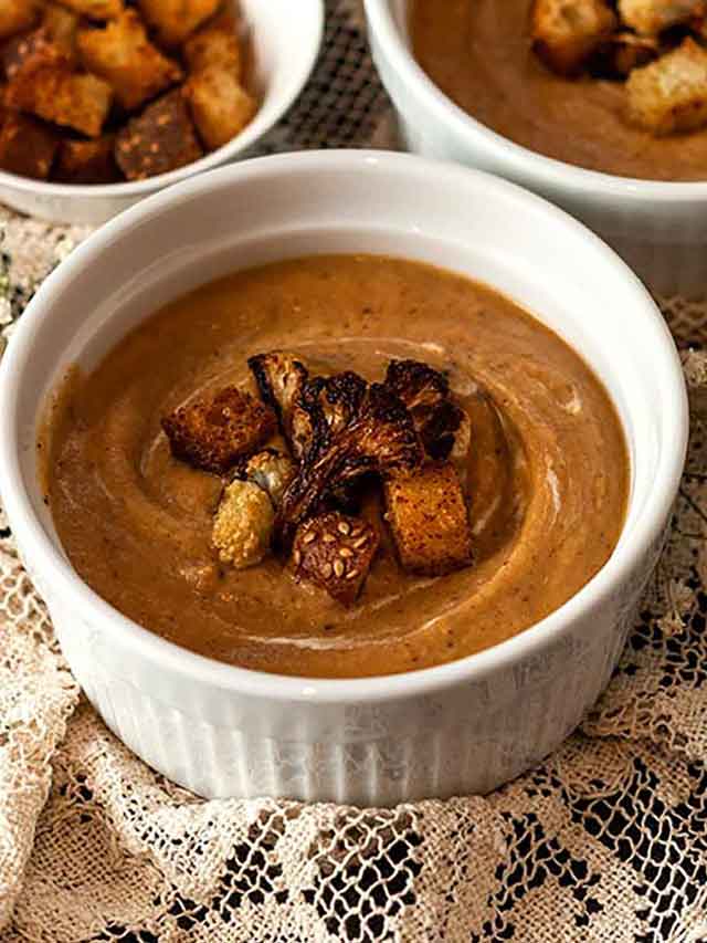 3 bowls of cauliflower soup and a small bowl of croutons on a lace table cloth.