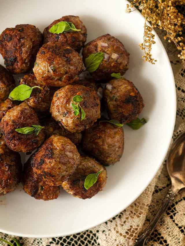 About 15 meatballs in a bowl, sprinkled with fresh oregano.