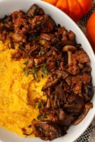 Pumpkin polenta with mushrooms in a bowl beside 2 small pumpkins.