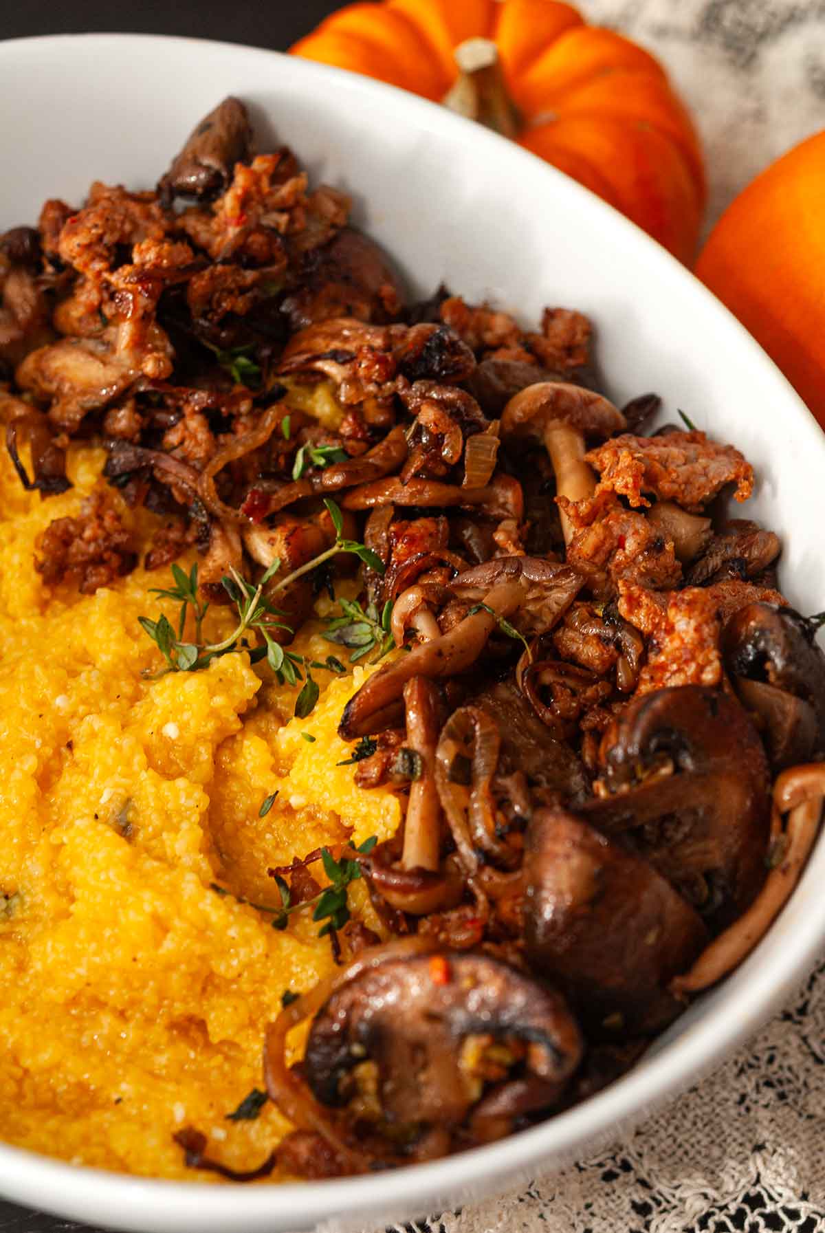 The mushrooms in a bowl of pumpkin polenta and mushrooms in front of 2 pumpkin gourds.