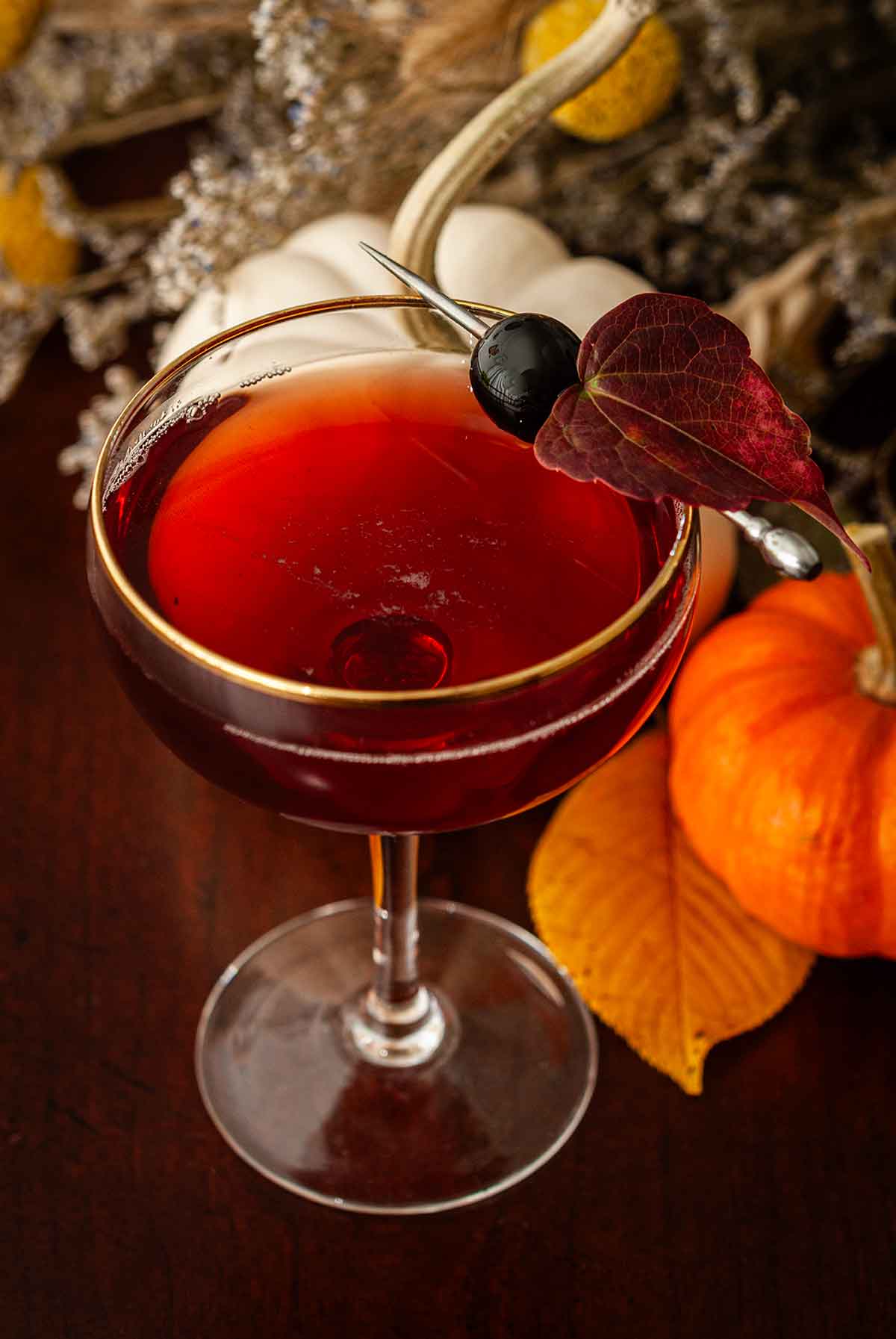 A cocktail in front of pumpkins, flowers and leaves on a table.